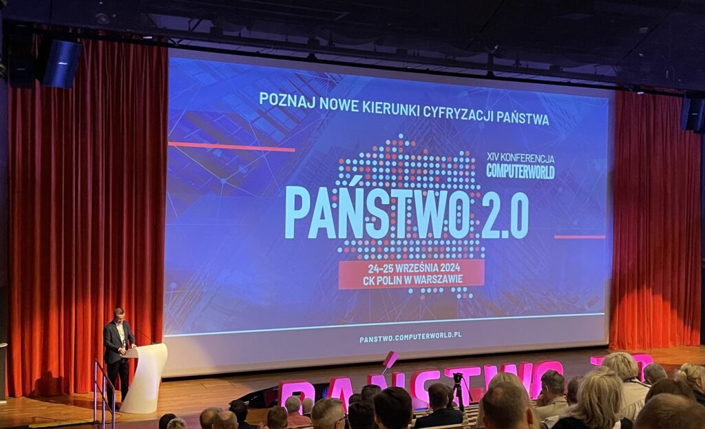 Sala konferencyjna pełna ludzi, w tle widać ekran z napisem Państwo 2.0